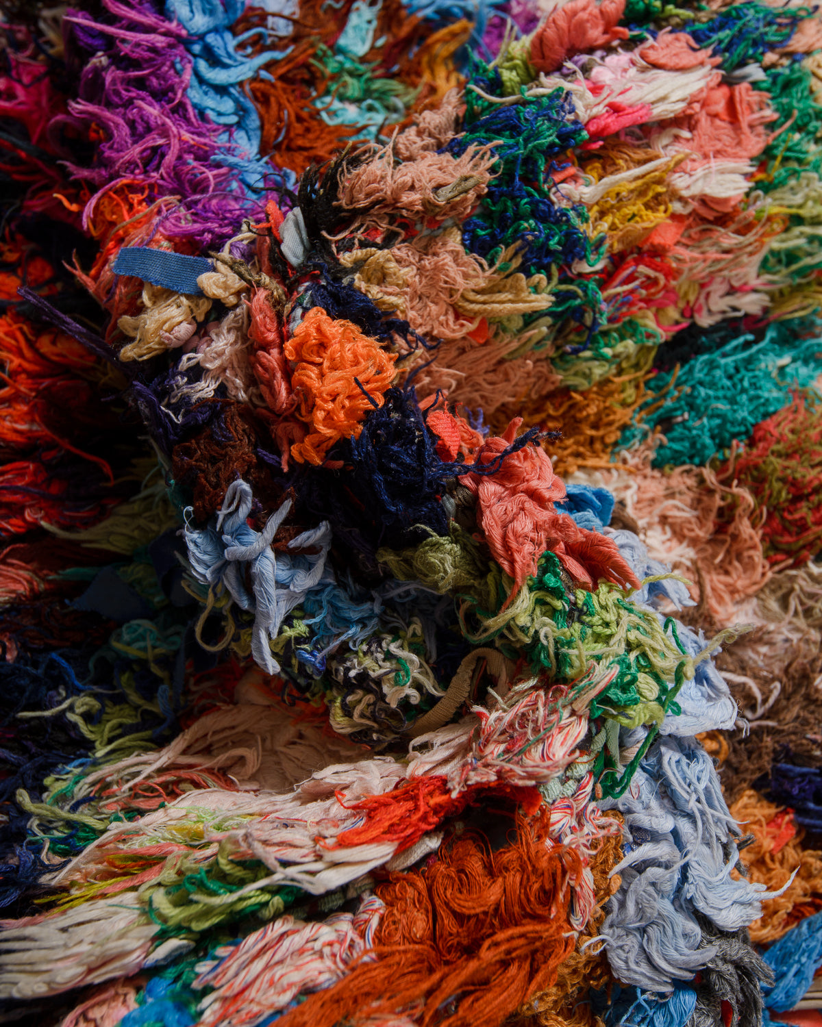 Close-up of a colorful textured fabric rug with various shades of orange, blue, green, and pink.